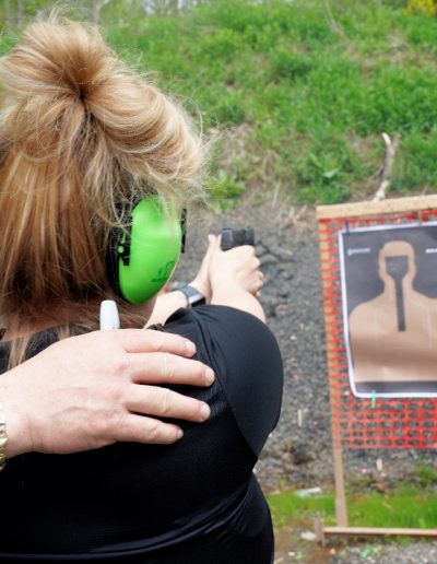 View behind person aiming firearm at paper target