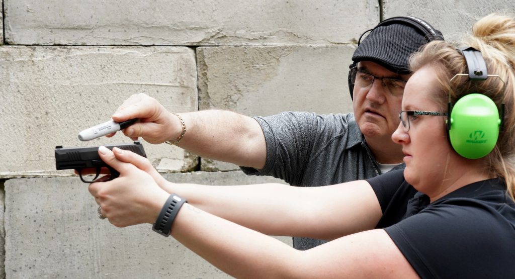 man pointing at gun while woman holds it