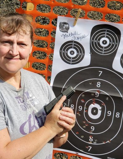 Person standing next to paper target with bullet holes